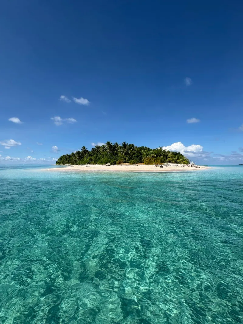 A tiny coral atoll surrounded by clear turquoise lagoon water.